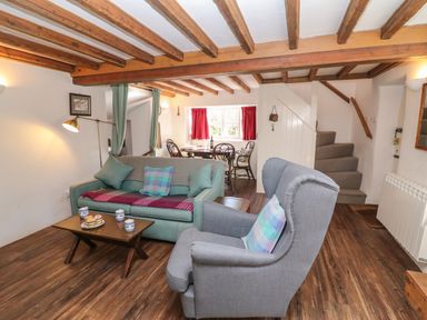 A living room with sofas a coffee table stairs and a dining area at Lychgate Cottage in Osmington