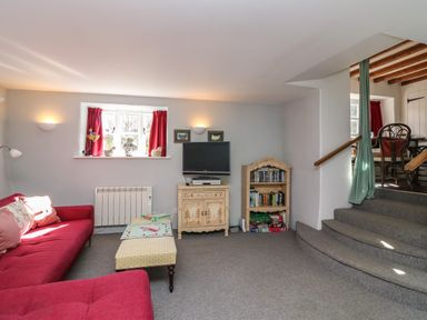 A living room with a red sofa a small cabinet with a tv a bookshelf and a table with board games at Lychgate Cottage in Osmington