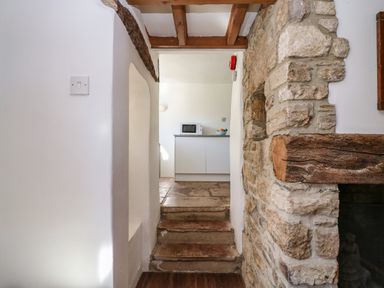 A stone wall and steps leading to a kitchen area with a microwave and fruit bowl at Lychgate Cottage in Osmington