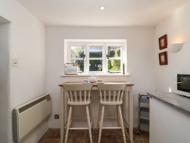 A small dining area with two white chairs and a wooden table under a window at Lychgate Cottage in Osmington