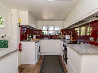 A kitchen with white cabinets red backsplash a washing machine oven and a sink at Lychgate Cottage in Osmington