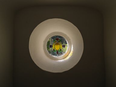 A circular stained glass window with colored patterns set in a thick white wall at Lychgate Cottage in Osmington