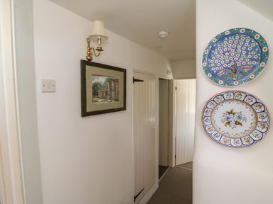 A hallway with white paneled doors a framed picture on the wall and decorative plates hanging at Lychgate Cottage in Osmington