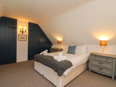 A bedroom with a double bed bedside tables lamps and dark blue built in cupboards at Lychgate Cottage in Osmington