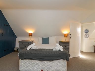 A bedroom with a double bed between two bedside tables with lamps and a blue door on the left at Lychgate Cottage in Osmington