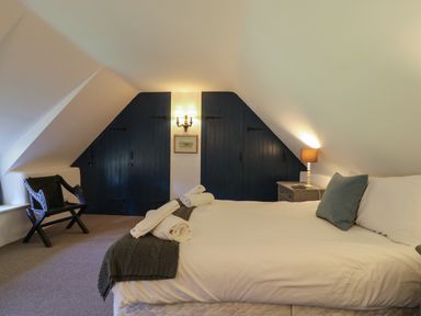 A bedroom with a bed towels on it a side table with a lamp and chair at Lychgate Cottage in Osmington
