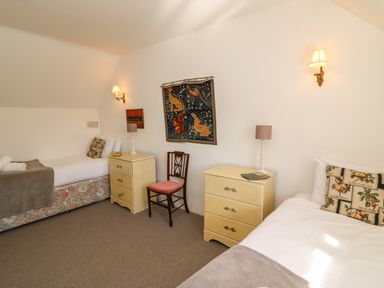 A bedroom with two single beds two cream bedside tables a wooden chair and animal wall hanging at Lychgate Cottage in Osmington
