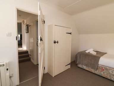 A small bedroom with a single bed and folded towels next to a white wooden door and a cupboard at Lychgate Cottage in Osmington