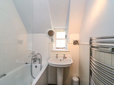A bathroom with a bathtub shower combination a pedestal sink a small window and a chrome towel heater at Lychgate Cottage in Osmington