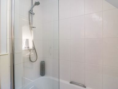 A bathroom with a bathtub and a showerhead mounted on the tiled wall at Lychgate Cottage in Osmington