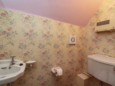 A bathroom with a sink toilet roll holder and wall-mounted heater at Lychgate Cottage in Osmington