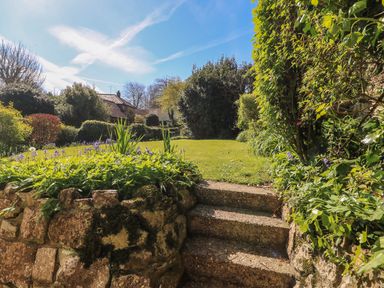 Stone steps leading up to a garden with grass and plants at Lychgate Cottage in Osmington