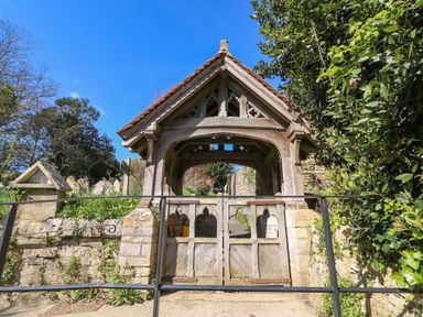 A wooden lychgate with a tiled roof and closed gates at Lychgate Cottage in Osmington