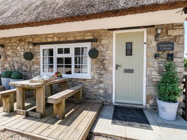 An outdoor wooden table with benches and a tea set in front of a stone cottage with a light green door at Magnolia Cottage Osmington