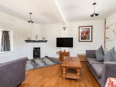 A living room with a wooden coffee table grey sofas a wall-mounted TV and a fireplace at Magnolia Cottage Osmington