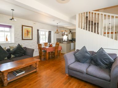 A living room and dining area with sofas, a wooden coffee table, dining table with chairs and kitchen in the background at Magnolia Cottage Osmington