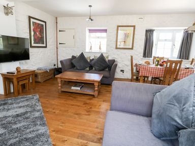A living room with sofas, a wooden coffee table, a television, a dining table with chairs and tableware at Magnolia Cottage Osmington