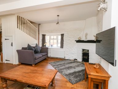 A living room with a gray sofa a wooden coffee table a patterned rug a fireplace and a wall-mounted television at Magnolia Cottage Osmington