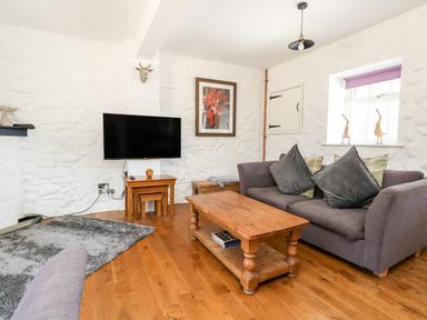 A living room with a gray sofa wooden coffee table flat screen tv on a stand and a window with purple blinds at Magnolia Cottage Osmington