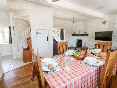 A dining area with a red checkered tablecloth on the table set with bowls bread and a fruit bowl in a room with white textured walls at Magnolia Cottage Osmington
