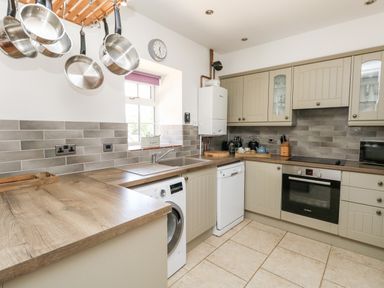 A kitchen with hanging pots and pans washing machine dishwasher oven and countertop at Magnolia Cottage Osmington
