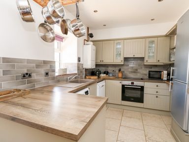 A kitchen with hanging pots, wooden countertops, grey cabinets, an oven, microwave, dishwasher, and a refrigerator at Magnolia Cottage Osmington