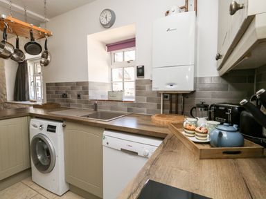A kitchen with washing machine dishwasher sink and countertop with tea set and cupcakes at Magnolia Cottage Osmington