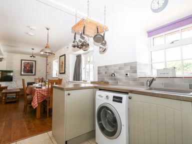 A kitchen and dining area with a washing machine under the counter and pans hanging above at Magnolia Cottage Osmington