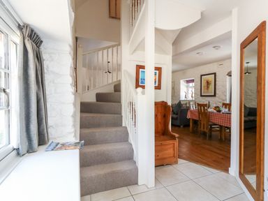 A hallway with stairs grey curtains and a mirror next to a dining area with a table and chairs at Magnolia Cottage Osmington