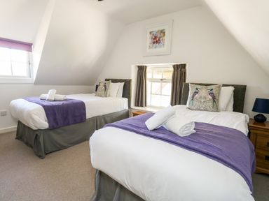 A bedroom with two single beds with purple throws and bird pillows a window between the beds and a small painting above at Magnolia Cottage Osmington