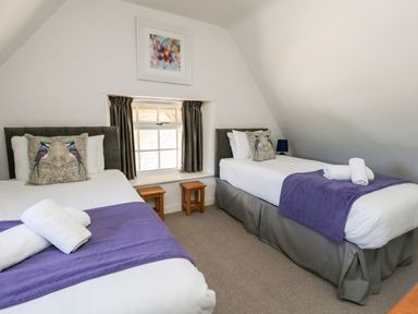 A bedroom with two single beds, each with a purple throw and bird pillows at Magnolia Cottage Osmington