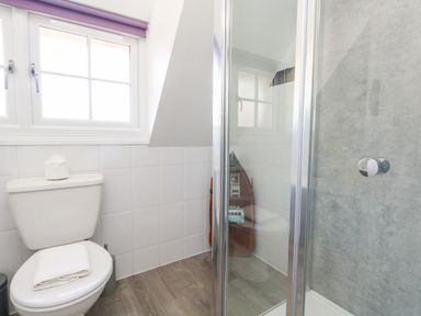 A bathroom with a toilet beside a window and a glass shower enclosure at Magnolia Cottage Osmington