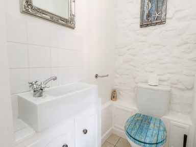 A bathroom with a white sink, a toilet with a blue wooden seat, and white tiled and stone walls at Magnolia Cottage Osmington