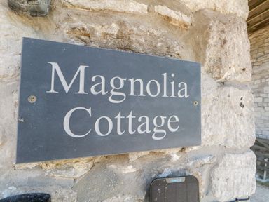 A stone wall with a sign that reads Magnolia Cottage at Magnolia Cottage Osmington in Osmington
