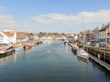A harbor with boats docked along both sides and buildings lining the waterfront at Magnolia Cottage Osmington