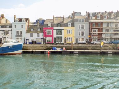 A harbor with a blue boat and colorful buildings along the waterfront at Magnolia Cottage Osmington