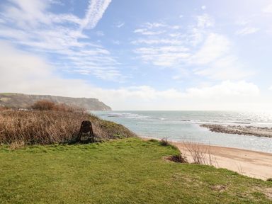 A coastal landscape with grass in the foreground a sandy beach sea and cliffs in the distance at Magnolia Cottage Osmington