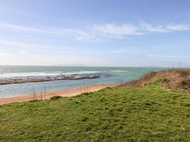 A grassy area overlooking a sandy beach and the sea with a blue sky at Magnolia Cottage Osmington