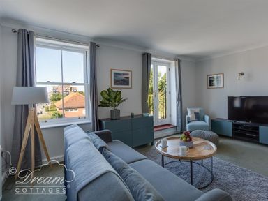 A living room with a blue sofa a round wooden coffee table a floor lamp a blue cabinet a television and windows with gray curtains at Marina Vista in Weymouth