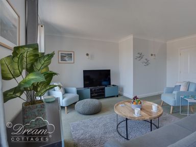A living room with two blue armchairs a grey pouf a wooden coffee table a television and a plant at Marina Vista in Weymouth
