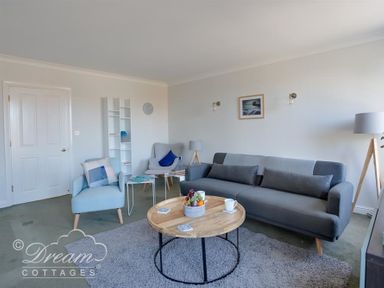 A living room with gray sofa blue armchairs round wooden coffee table and white shelving unit at Marina Vista in Weymouth