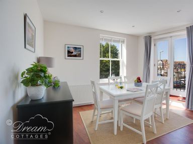 A dining area with white table and chairs near window and glass doors with cabinet and plant at Marina Vista in Weymouth