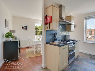 A kitchen with a gas stove and blue tiled backsplash next to a dining area with a white table and chairs at Marina Vista in Weymouth