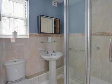 A bathroom with a toilet a pedestal sink a wall-mounted mirror cabinet a glass shower enclosure and a window with blinds at Marina Vista in Weymouth