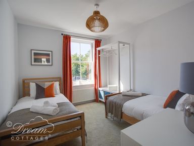 A bedroom with two single beds a window with orange curtains and a white open wardrobe at Marina Vista in Weymouth