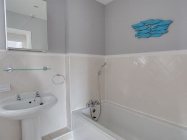 A bathroom with a pedestal sink bathtub showerhead and fish wall decoration at Marina Vista in Weymouth