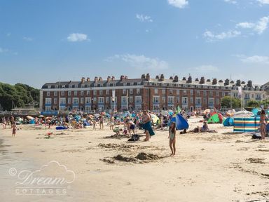 A crowded beach with people and tents in front of a large brick building at Marina Vista in Weymouth