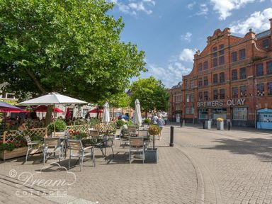 An outdoor seating area with tables umbrellas and chairs next to a large brick building with sign Brewers Quay at Marina Vista in Weymouth