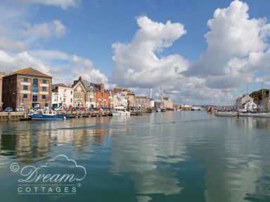 A harbor with boats docked along the waterfront and buildings lining the quay at Marina Vista in Weymouth