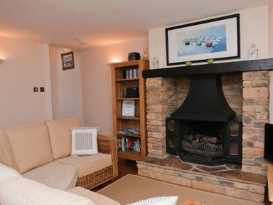 A living room with a beige sofa a stone fireplace a wooden bookshelf and a framed picture above the fireplace at Courtyard House Dartmouth